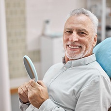 a person smiling and holding a mirror in their hands while sitting in a dental treatment chair