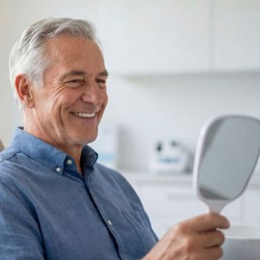 Happy senior patient looking at his smile in mirror