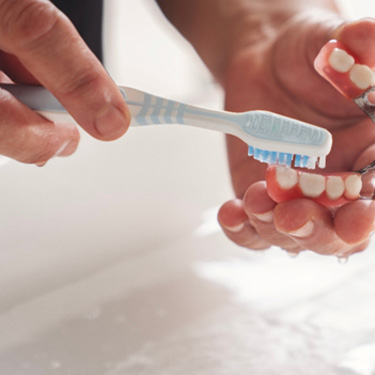 Hands brushing a partial set of dentures