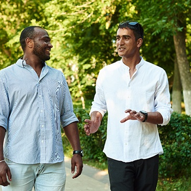 Two men outside walking and talking near trees