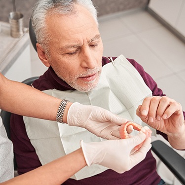 Dentist handing dentures to man in dental chair with red sweater