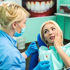A young female in the dentist’s chair and looking at her dentist for help