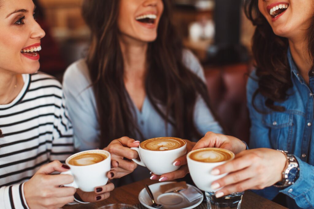 Three women at round wood table enjoying coffee and smiling